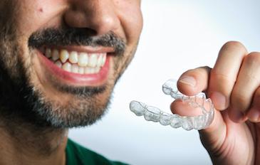 A smiling man holding an Invisalign tray
