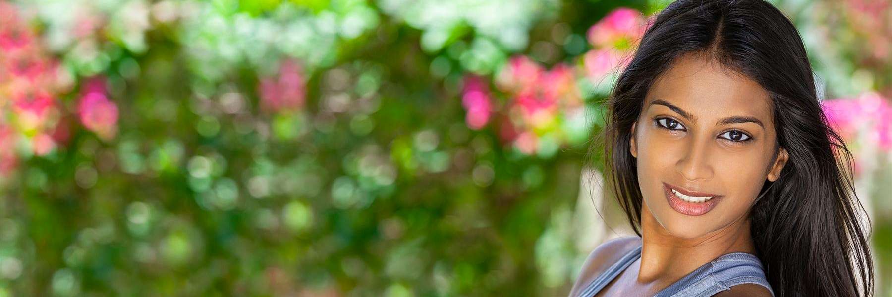 A smiling woman in front of a wall of flowers | dental implants Corona, CA