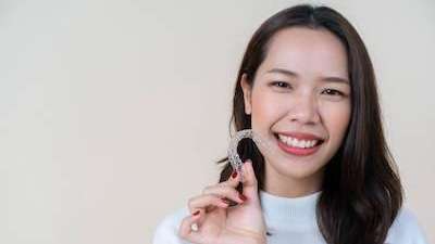 A smiling woman holding an Invisalign tray