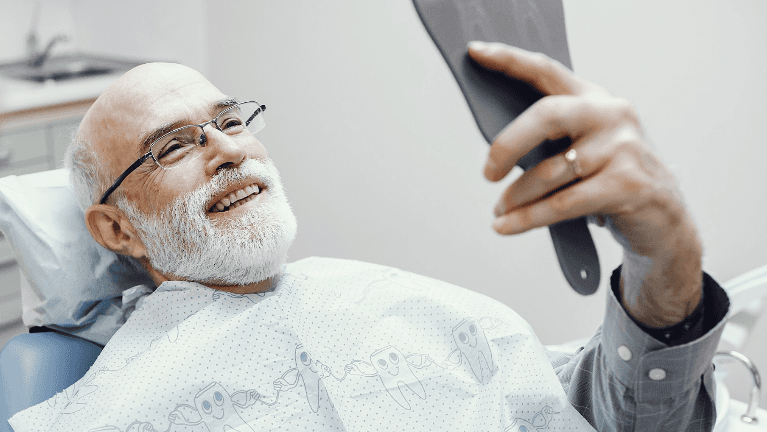 A smiling man looking at his dental implants in the mirror