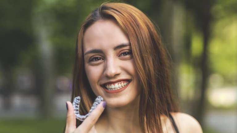 smiling woman holding Invisalign aligners