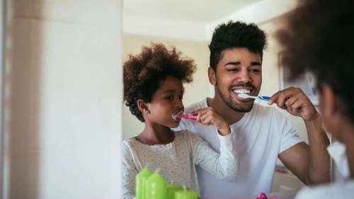 A father and daughter brushing their teeth in the mirror